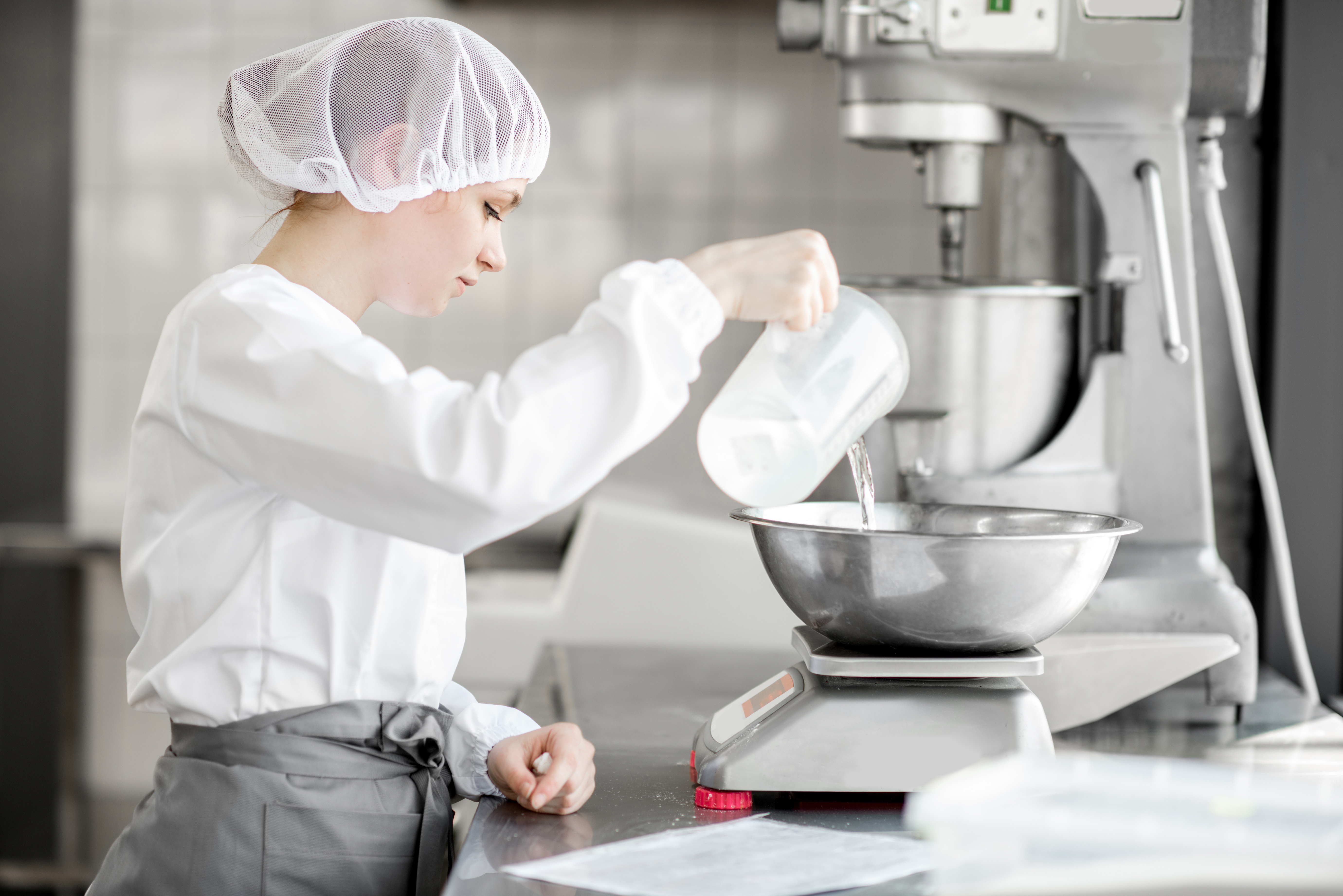 Woman confectioner in uniform weighing ingredients for pastry working at the bakery manufacturing